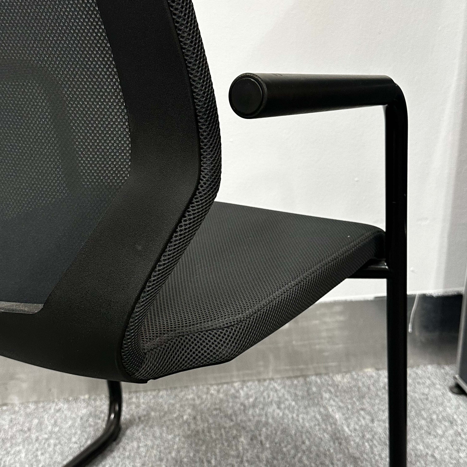 Close-up of black König+Neurath Konferenzstuhl with mesh seat and armrest in modern office setting