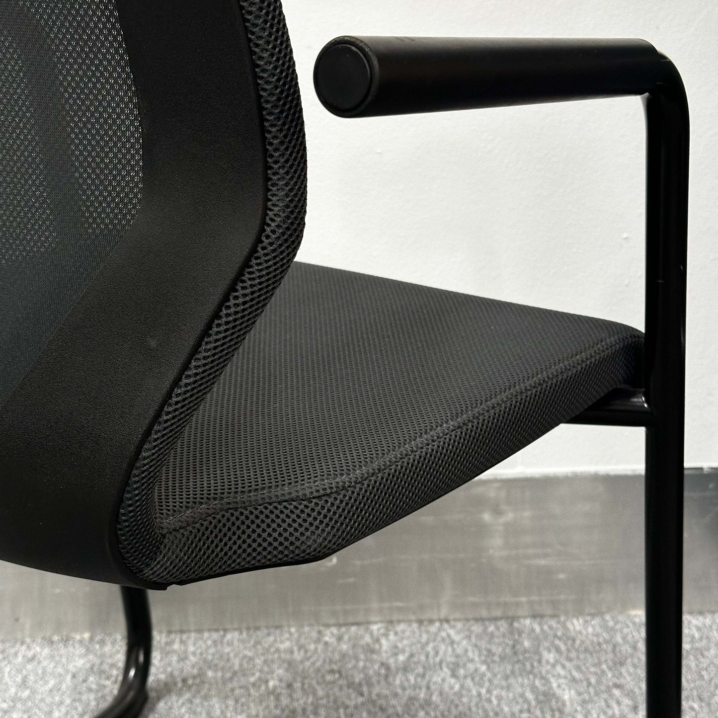 Close-up of König+Neurath Konferenzstuhl with black mesh seat and armrest in modern office setting
