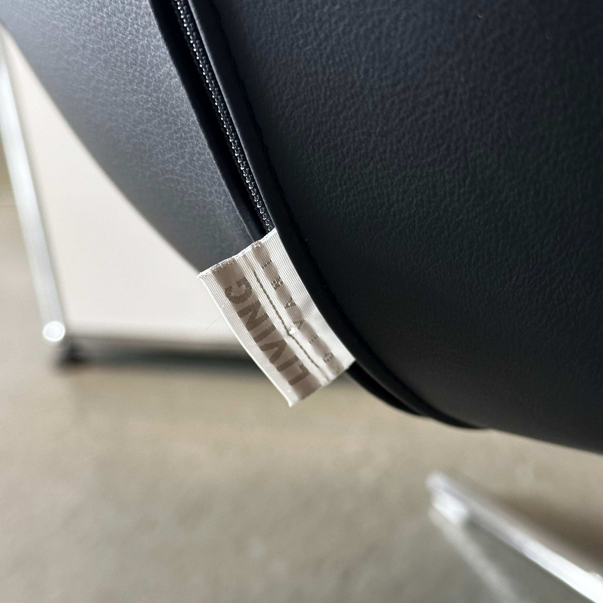 Close-up of black Living Divani Ledersessel Jelly leather armchair with tag and sleek metal legs.