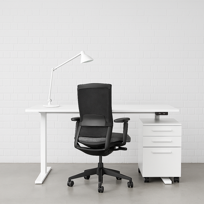 White EHV-1 elektrisch höhenverstellbarer Schreibtisch mit weißer Tischplatte, schwarzem Bürostuhl, Schreibtischlampe und weißem Rollcontainer vor weißer Backsteinwand.