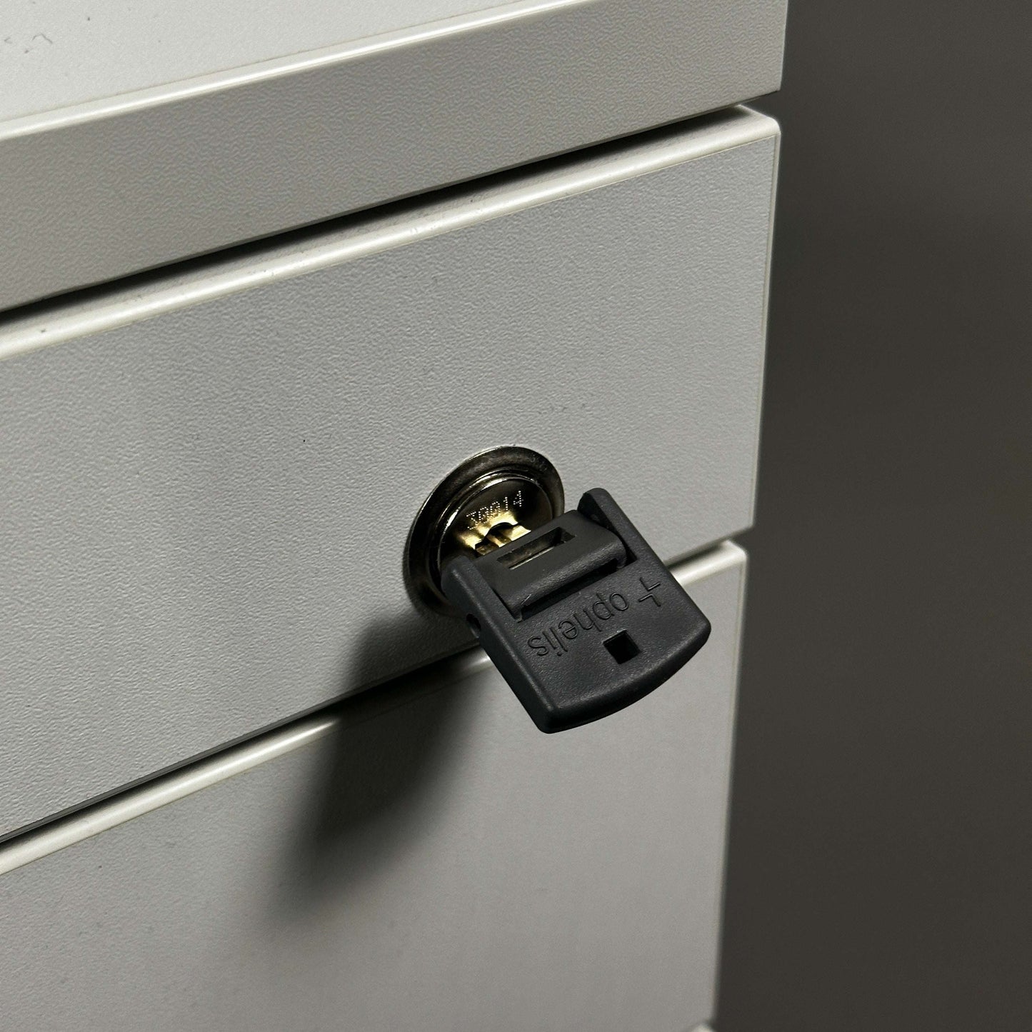 Nahaufnahme eines weißen, abschließbaren Ophelis Rollcontainers aus Holz mit Schlüssel im Schließzylinder