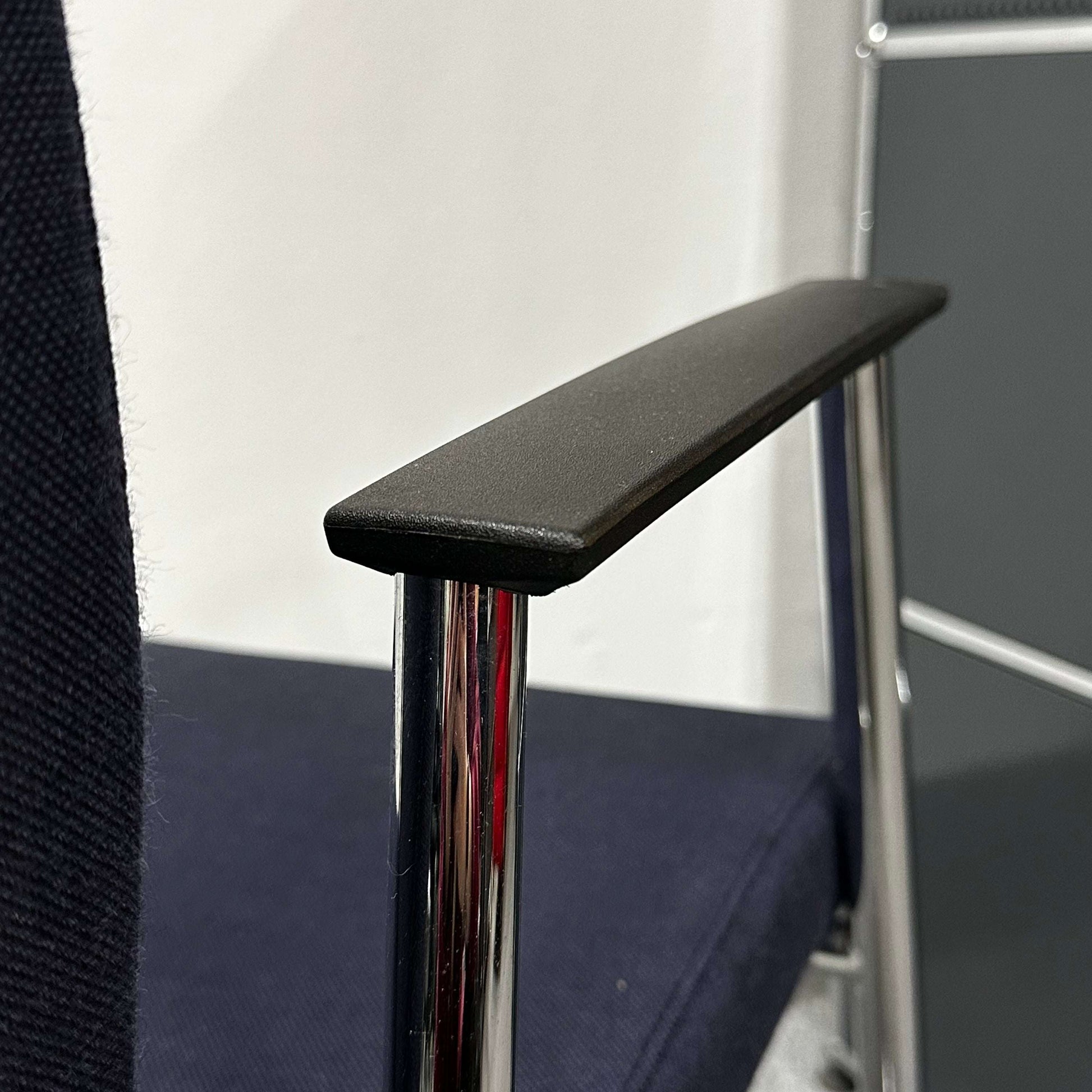 Close-up of Sedus Freischwinger chair's black armrest and chrome frame with dark blue fabric seat
