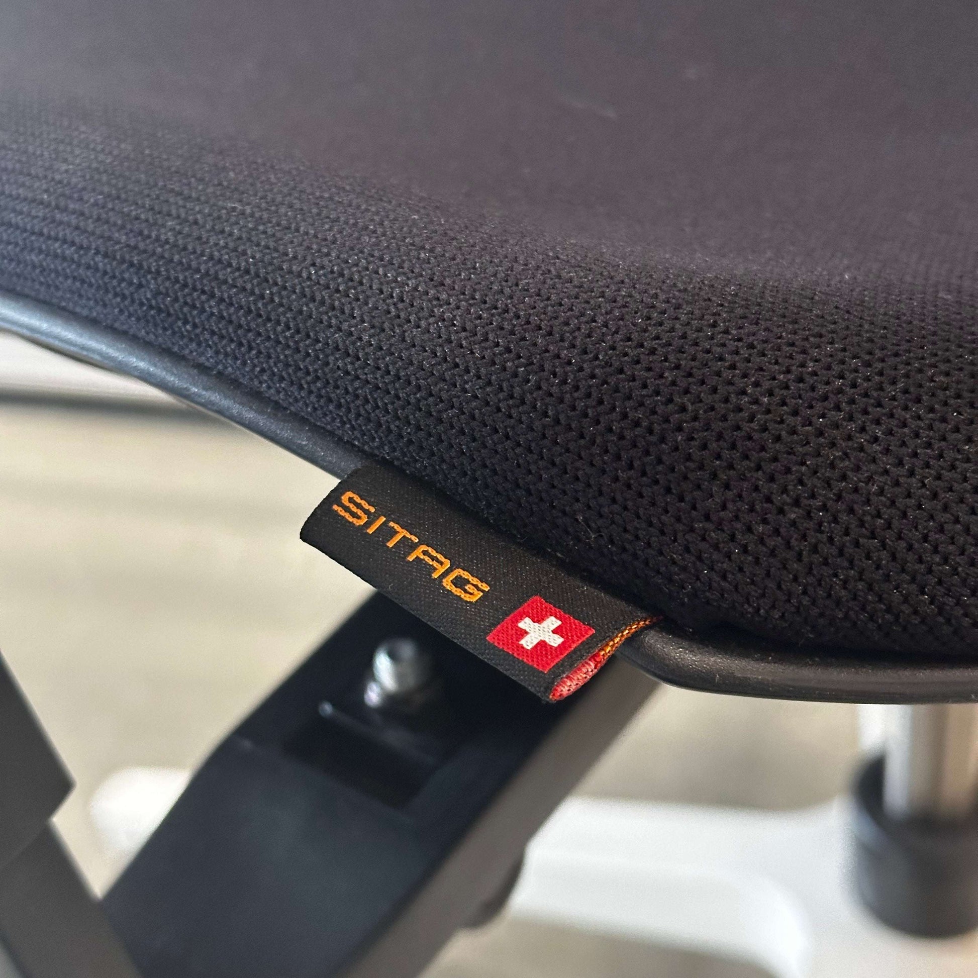 Close-up of black fabric and Sitag tag on a Sitag Wave ergonomic chair with white frame and adjustable features