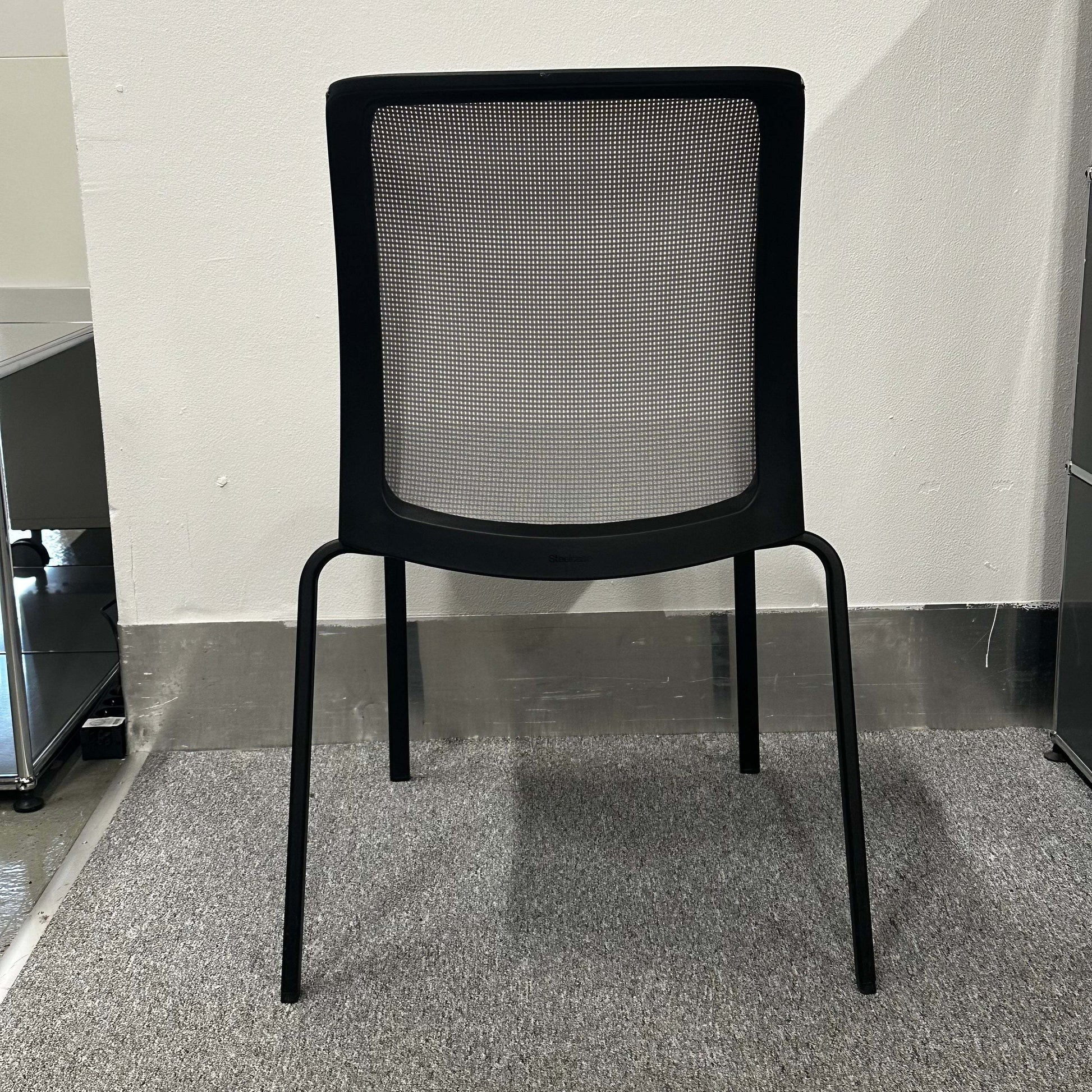 Black Steelcase Eastside Stapelstuhl with mesh backrest and four legs on carpeted floor