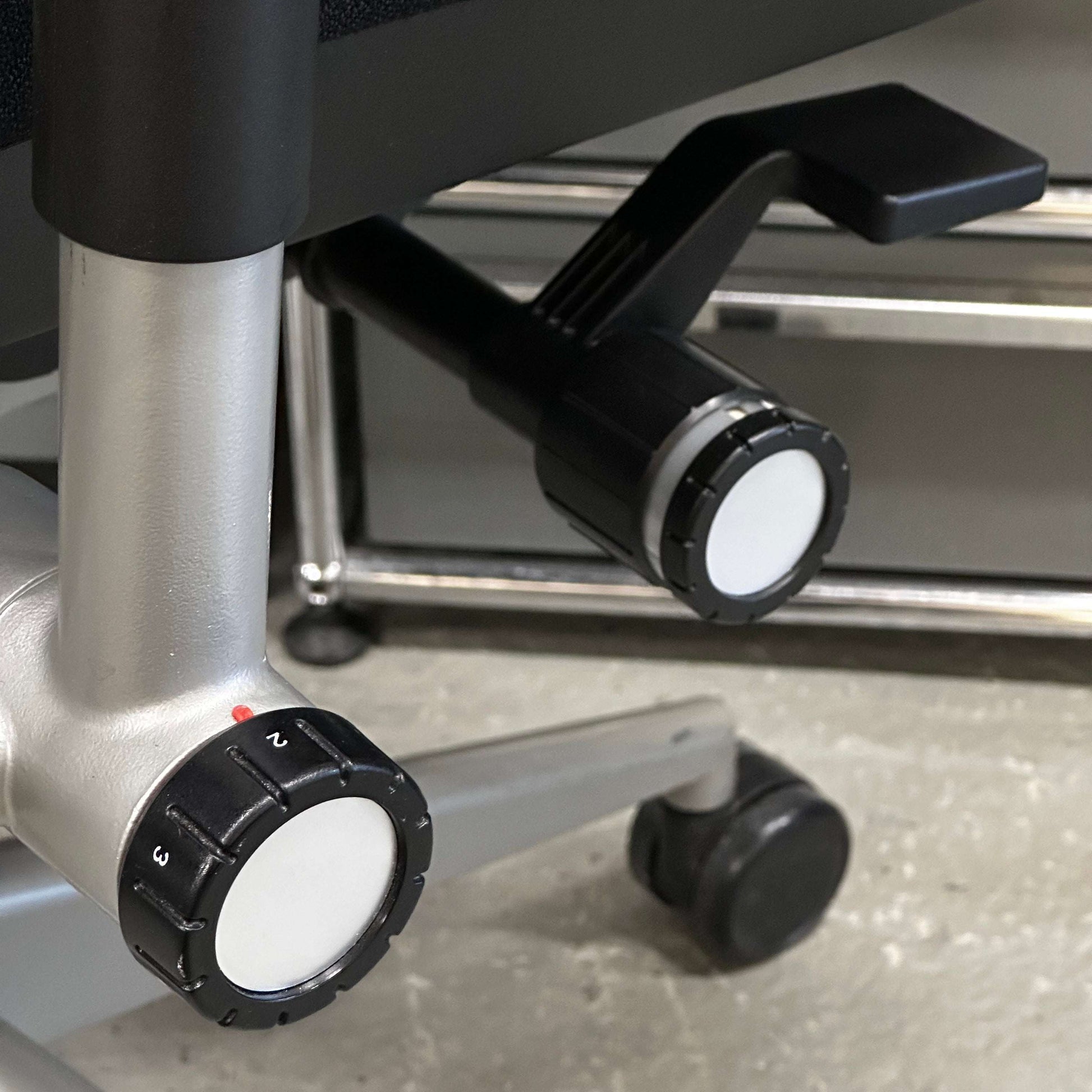 Close-up of adjustment knobs and lever on Steelcase Please ergonomic office chair base with wheels