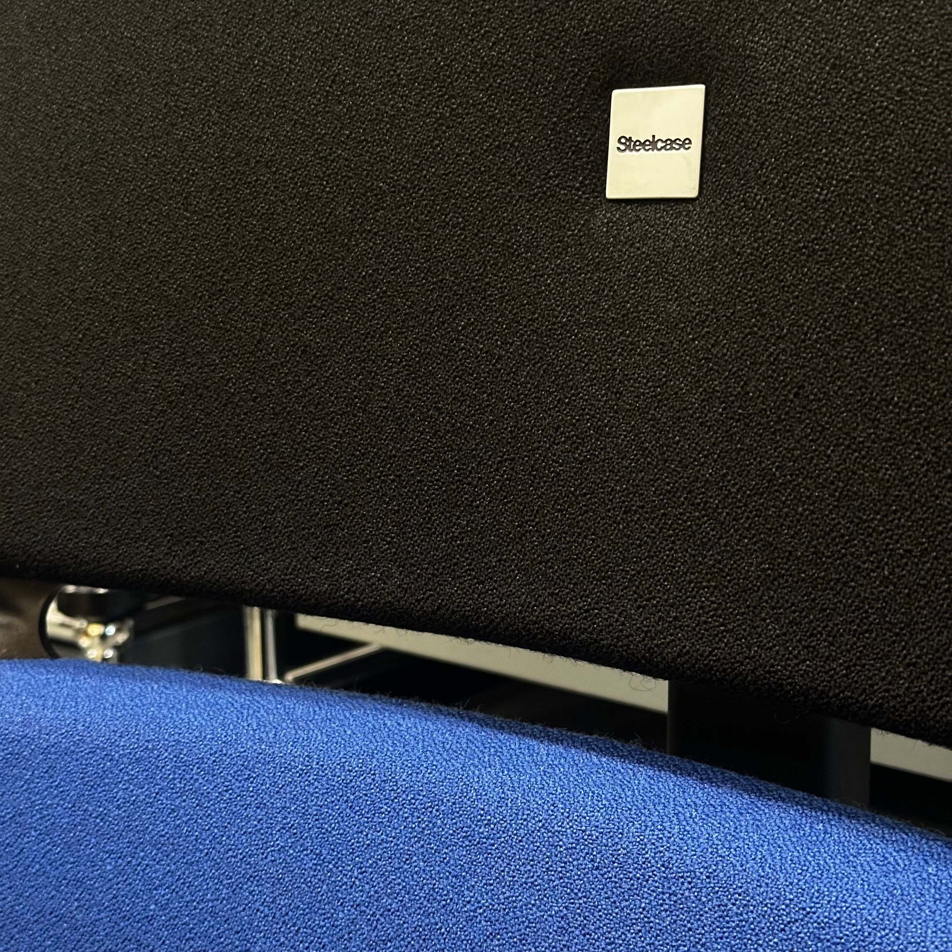 Close-up of Steelcase Please ergonomic office chair with black backrest and blue seat cushion showcasing modern design and comfort features.