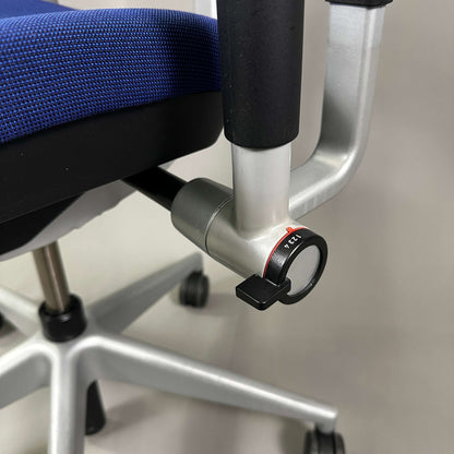 Close-up of adjustment knob on blue Steelcase Please ergonomic office chair with silver metal frame and caster wheels
