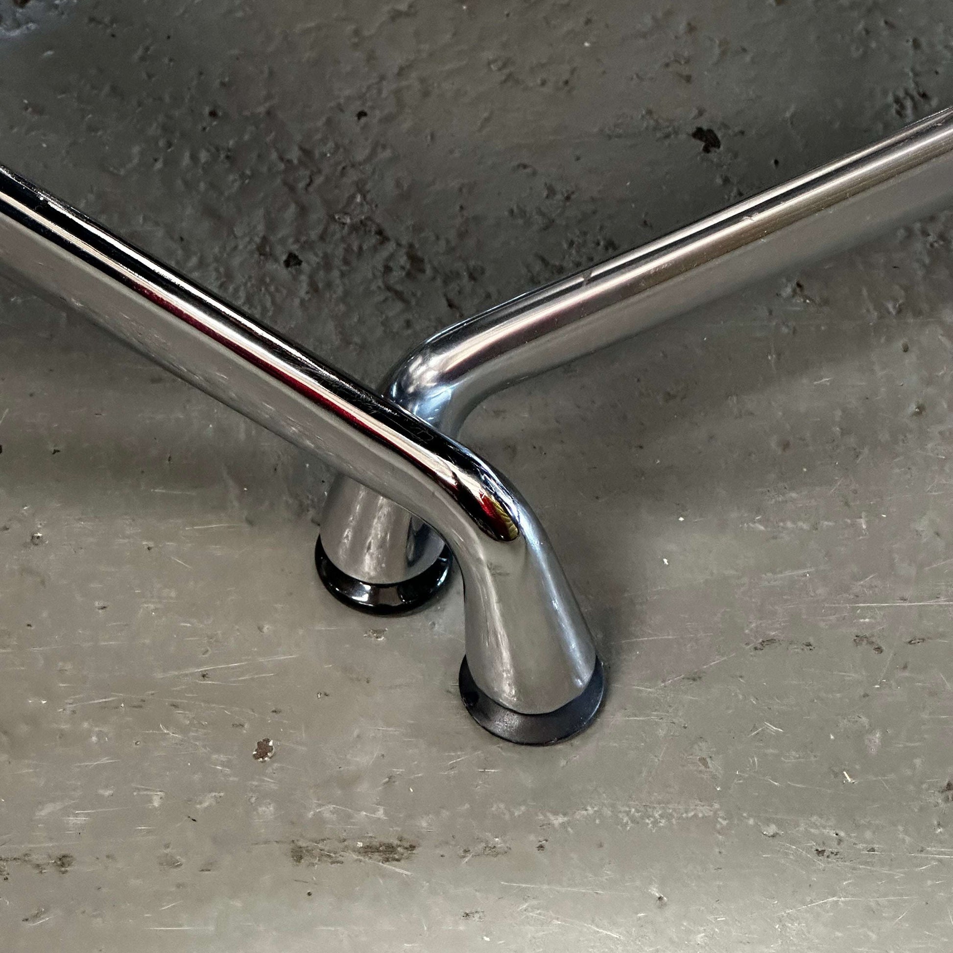 Close-up of chrome legs on black faux leather Stuhl im Vitra EA108 replica chair on concrete floor