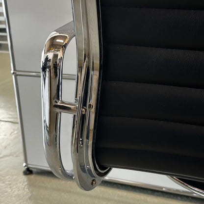 Close-up of black faux leather Stuhl im Vitra EA108 replica with chrome armrest detail