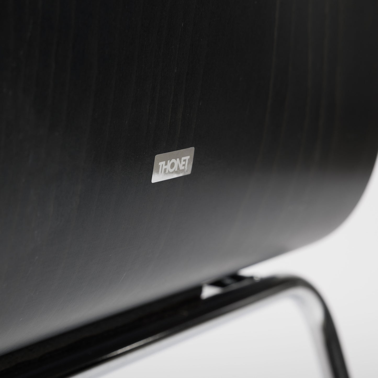 Close-up of a black Thonet S166 PF chair, showing the Thonet logo on the dark wood backrest.