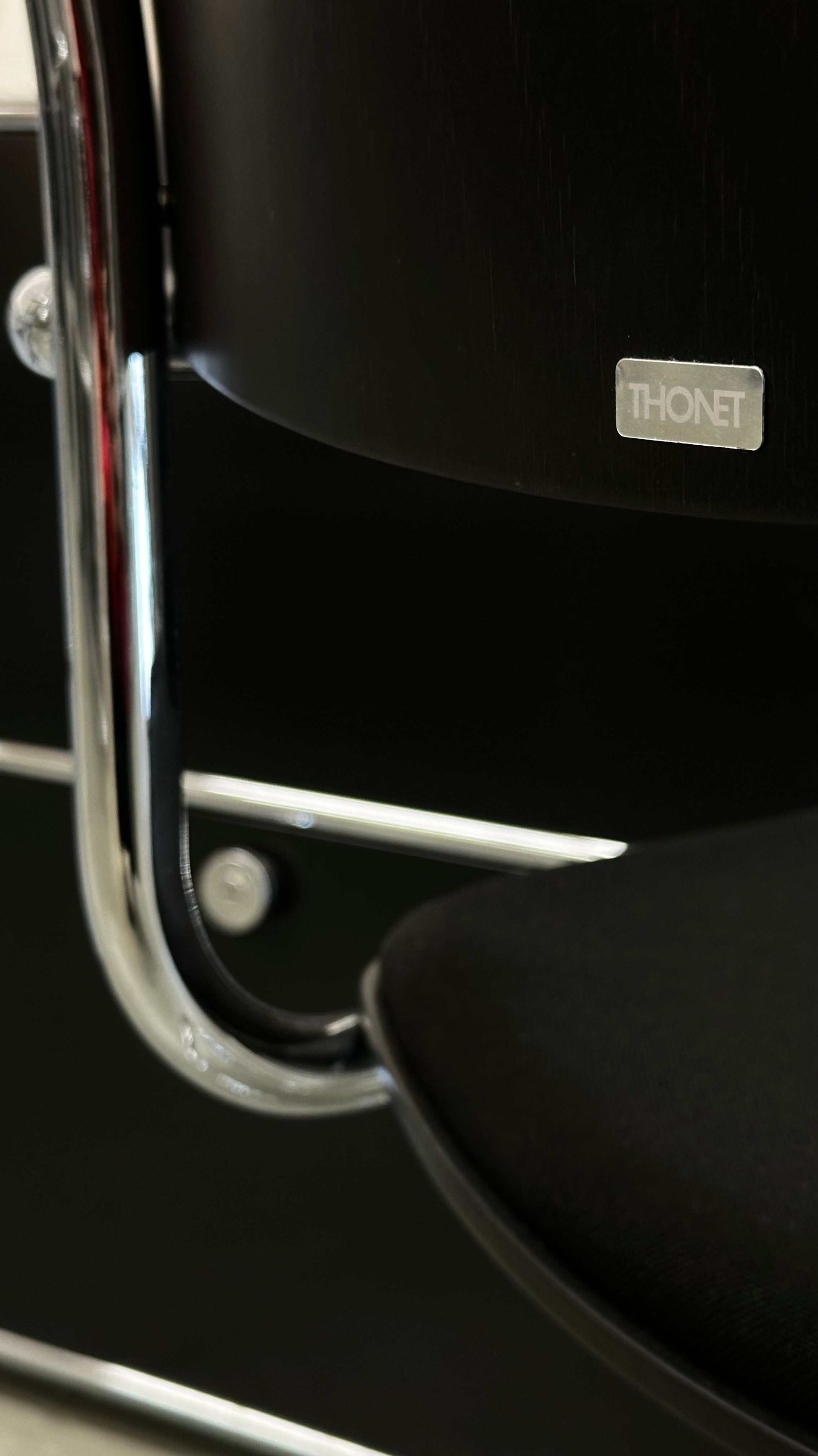Close-up of black Thonet S43 PVF chair with chrome frame and wooden armrest showing brand logo