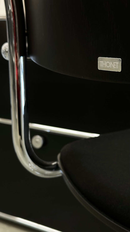 Close-up of black Thonet S43 PVF chair with chrome frame and wooden armrest showing brand logo