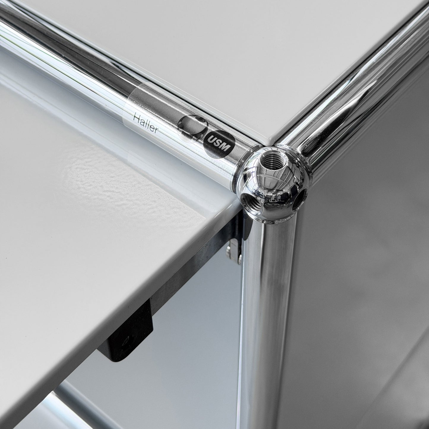 USM Haller 1x2 Sideboard in lichtgrau mit verchromten Rohren und Kugelverbindern, USM Logo sichtbar.