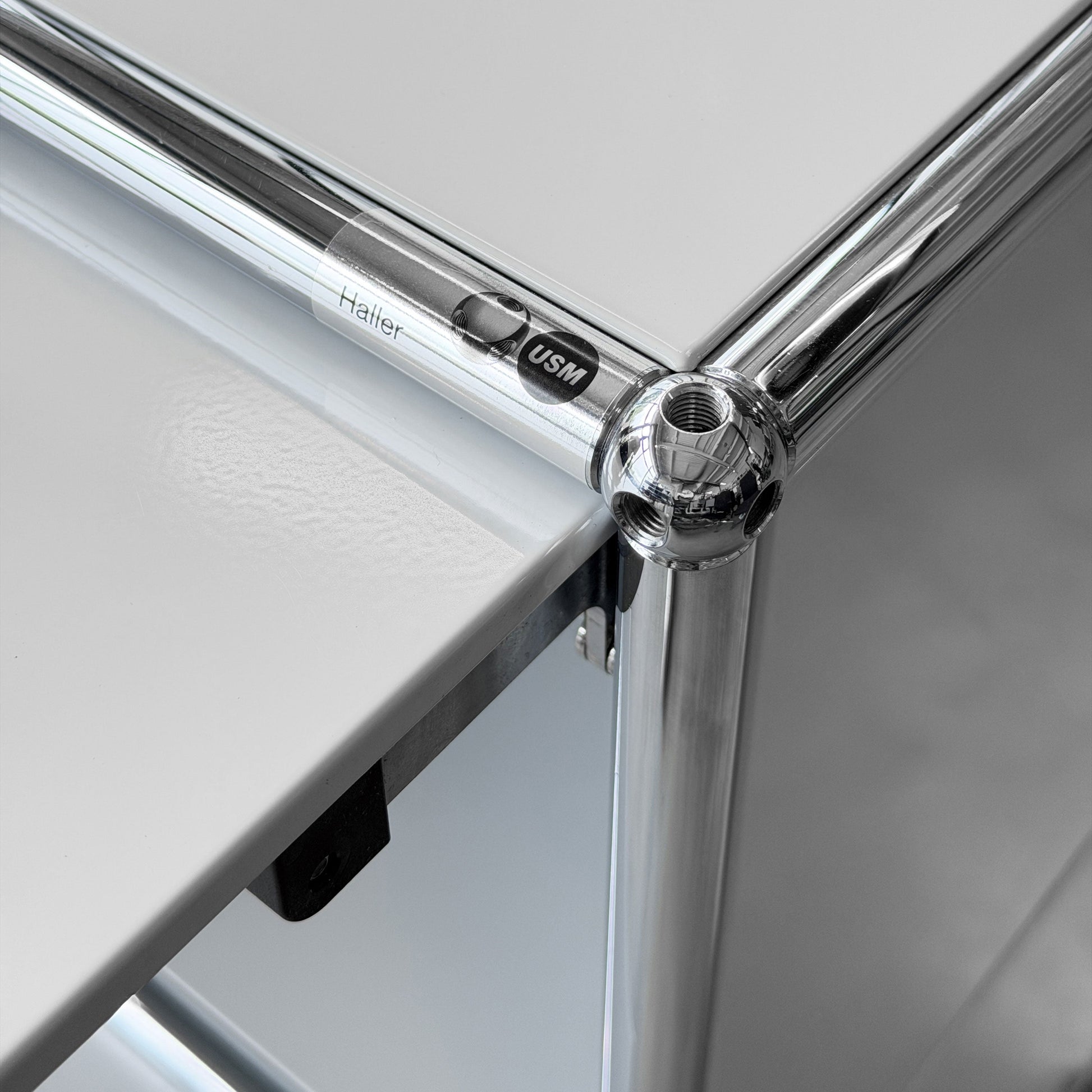 USM Haller 1x2 Sideboard in lichtgrau mit verchromten Rohren und Kugelverbindern, USM Logo sichtbar.