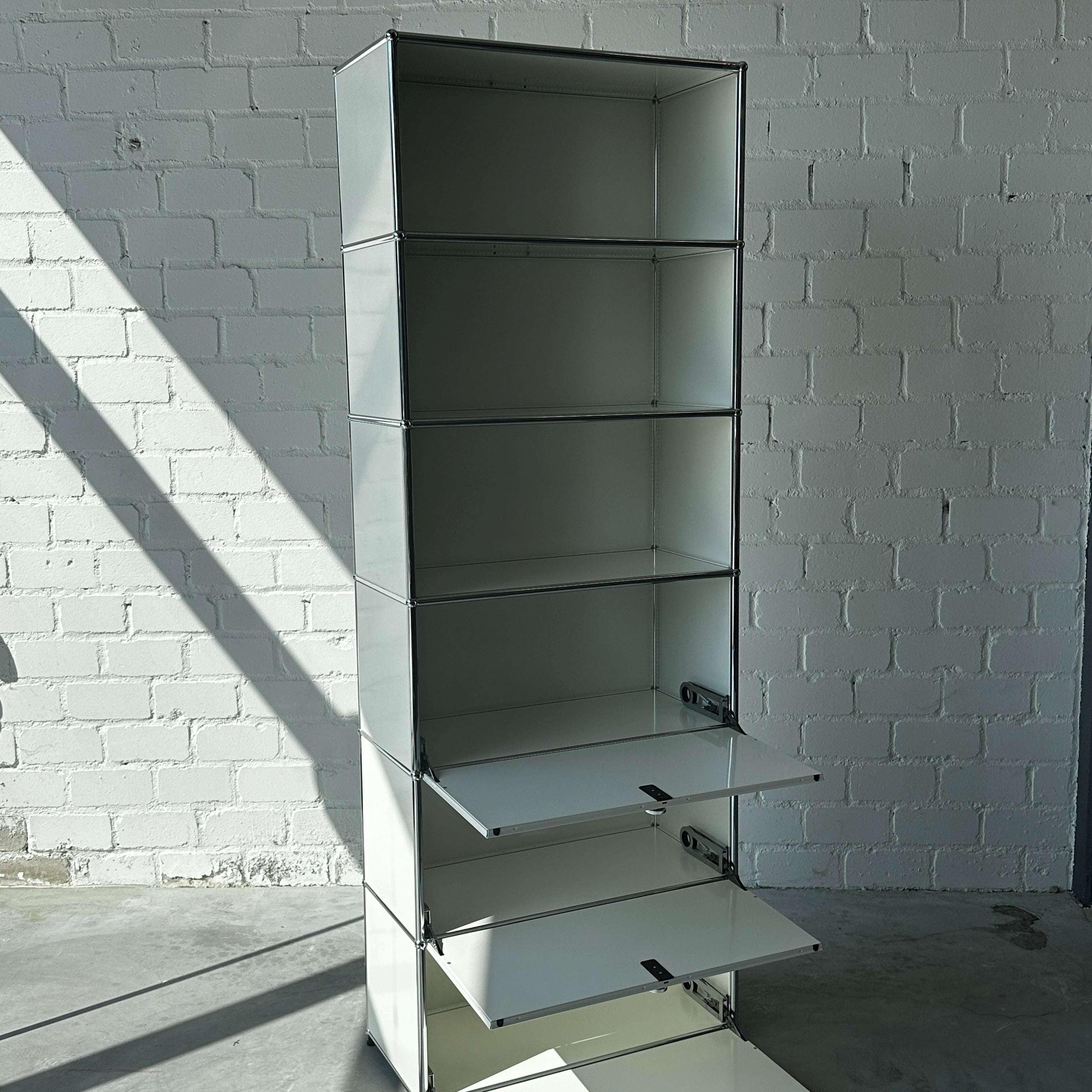 USM Haller 1x6 Highboard weiß mit 3 Klappen und offenem Regal vor weißer Ziegelwand