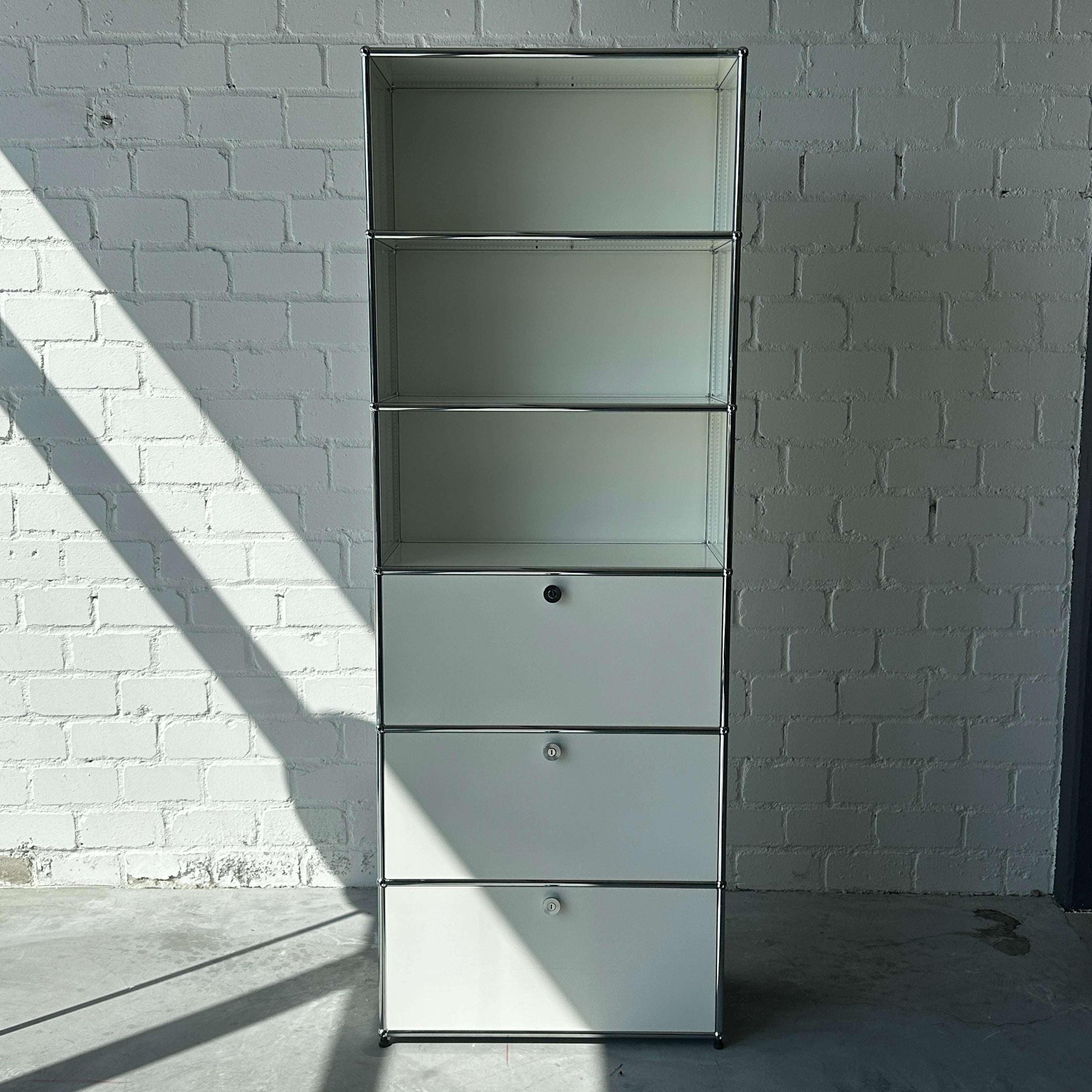 USM Haller 1x6 Highboard weiß mit 3 Klappen vor weißer Ziegelwand und Schatten