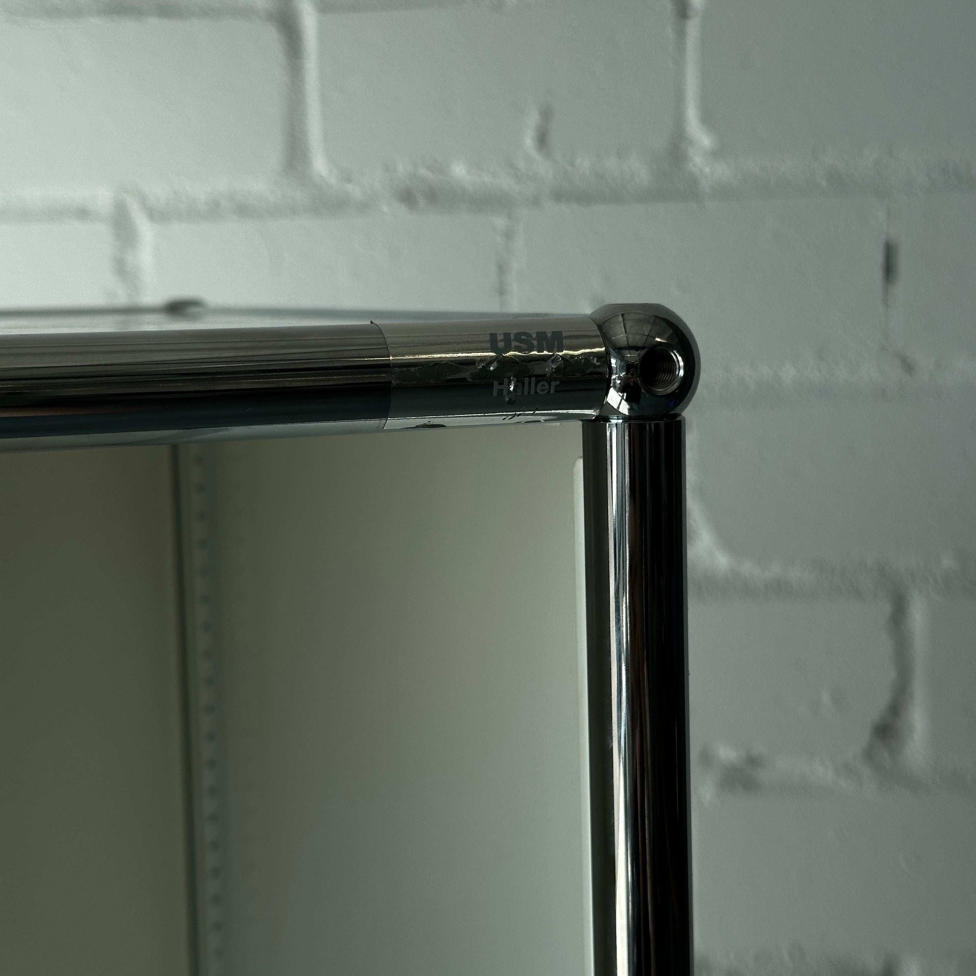 USM Haller 1x6 Highboard weiß mit drei Klappen und verchromtem Rahmen vor weißer Ziegelwand