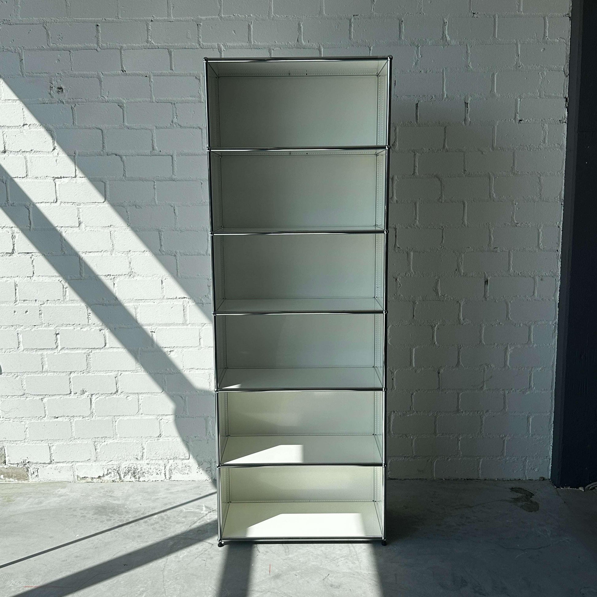 USM Haller offenes weißes 1x6 Highboard Regal vor weißer Backsteinwand mit Sonnenschein