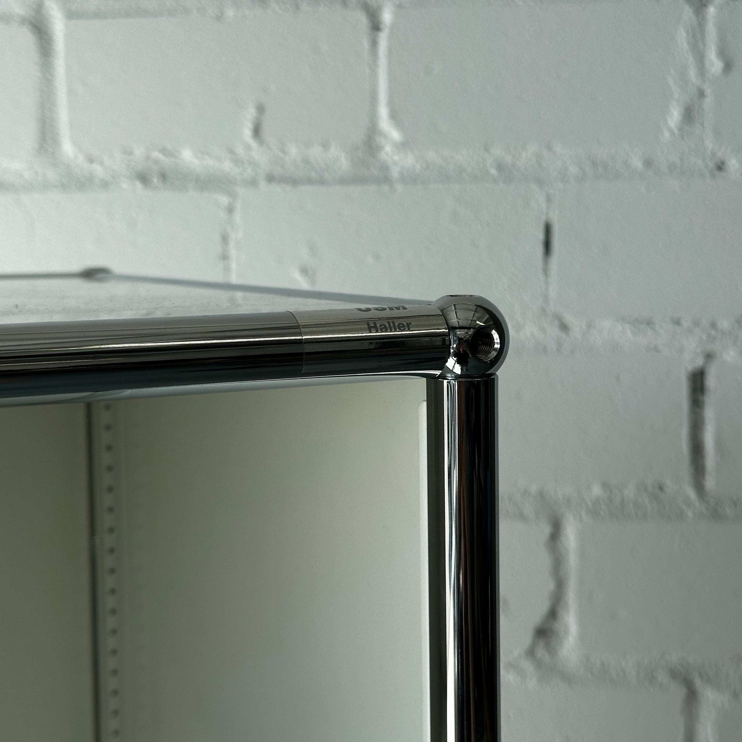 USM Haller 1x6 Highboard weiß offen mit verchromtem Rahmen vor weißer Backsteinwand