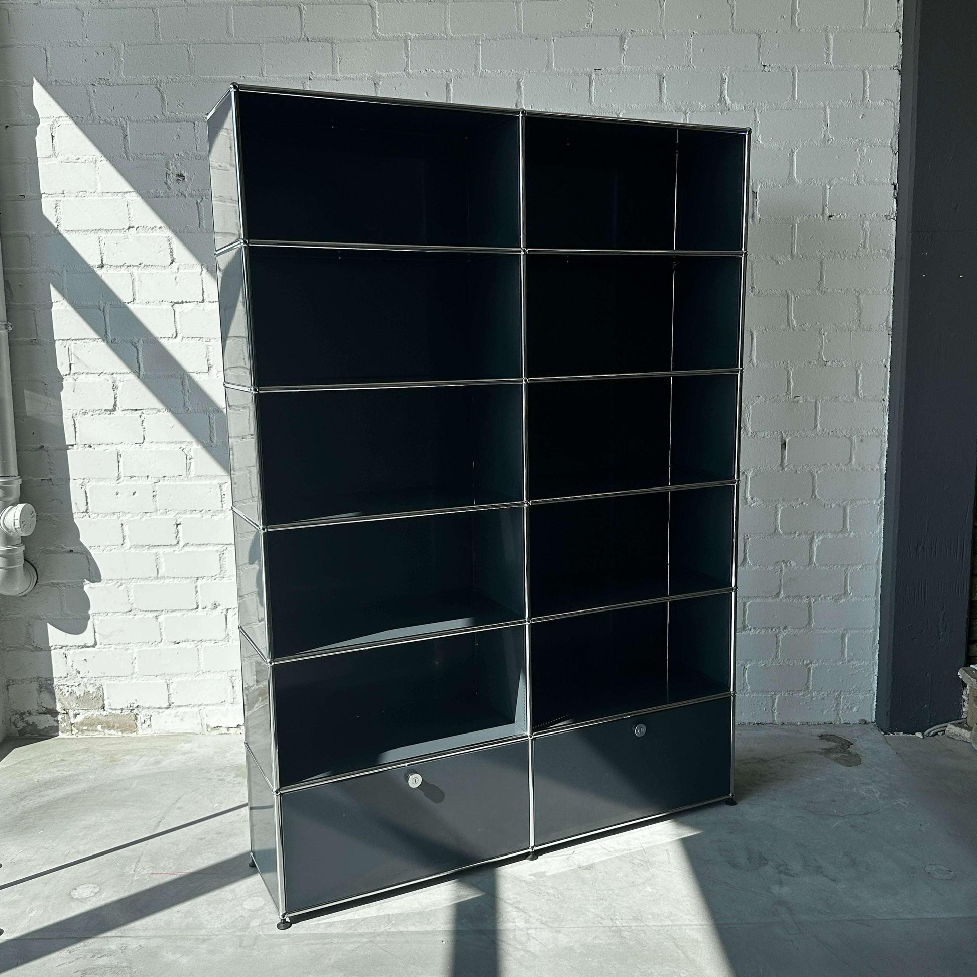 USM Haller 2x6 Highboard in Anthrazitgrau mit zwei Schubladen und offenen Fächern vor weißer Backsteinwand