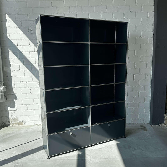 USM Haller 2x6 Highboard in Anthrazitgrau mit zwei Schubladen und offenen Fächern vor weißer Backsteinwand