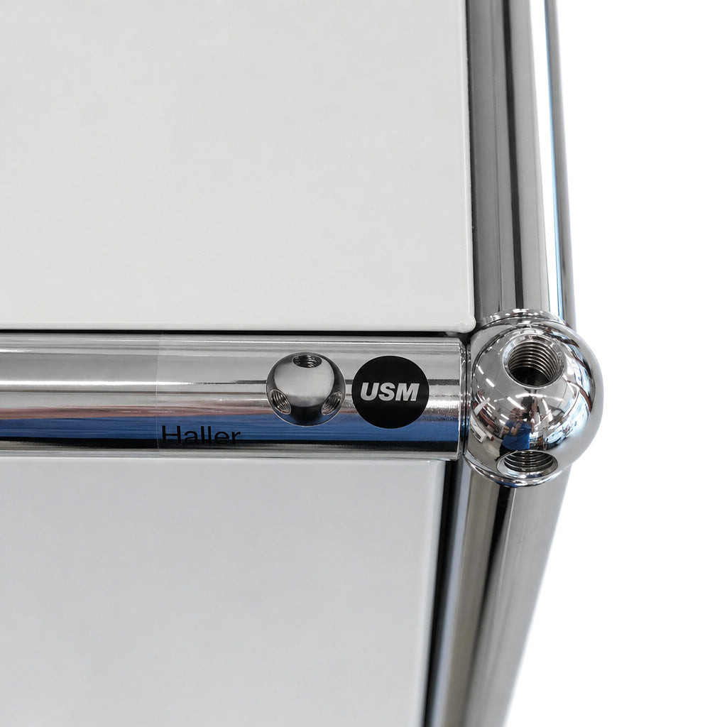 Detailansicht eines USM Haller Highboards in Lichtgrau mit charakteristischer Chrom-Struktur und USM-Markenlogo.