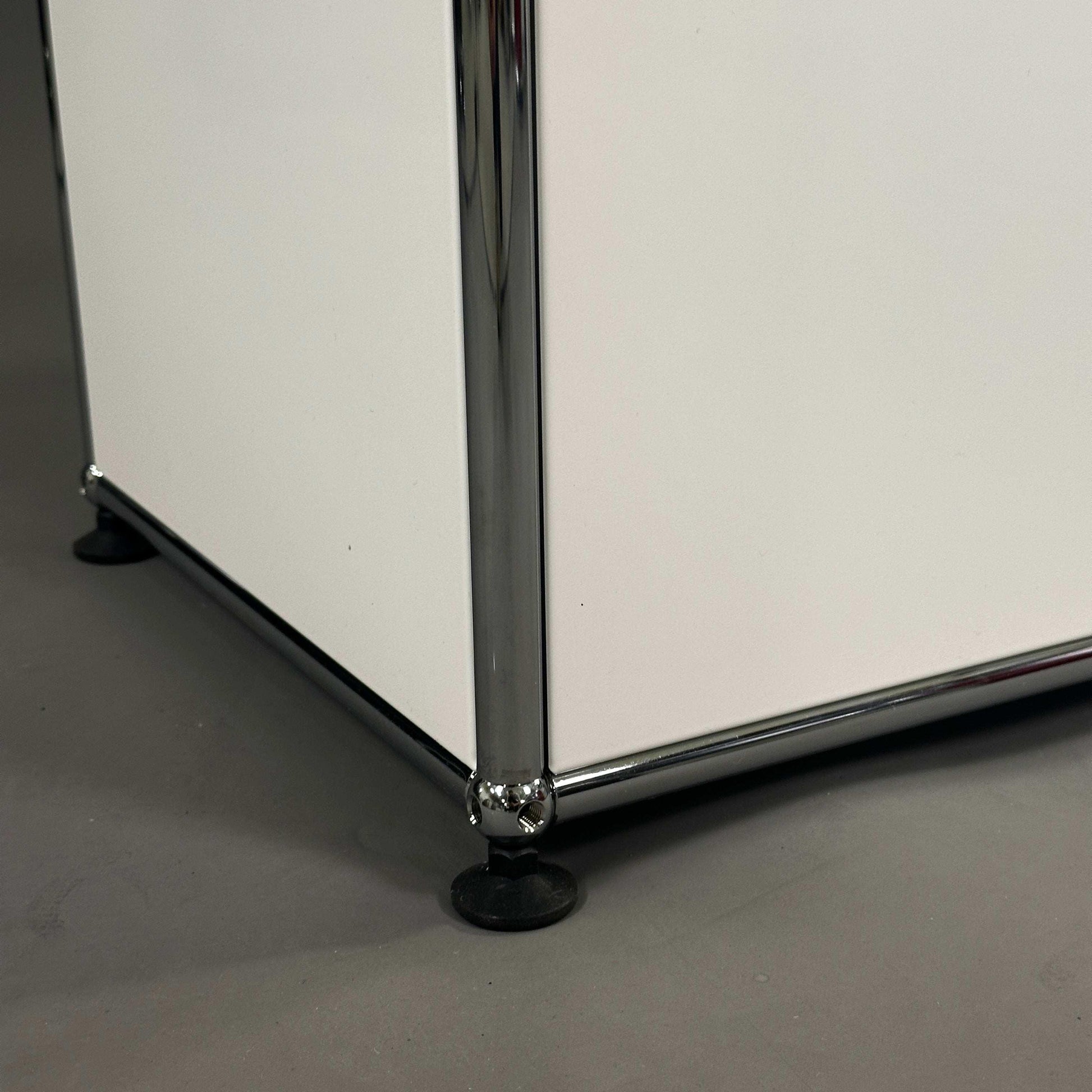 Detailaufnahme der unteren Ecke eines weißen USM Haller Highboards mit Chrom-Stahlrahmen und verstellbarem Fuß