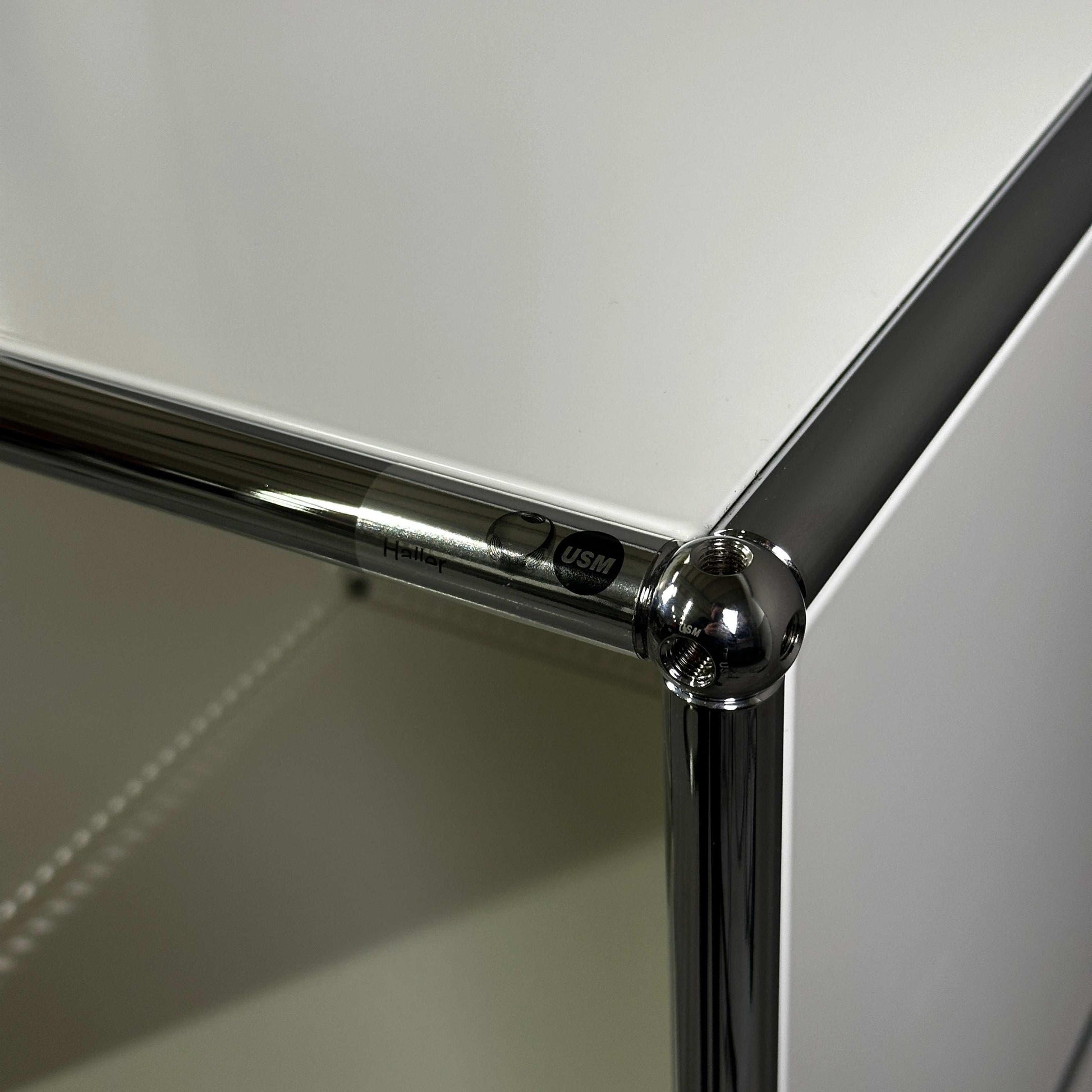 Nahaufnahme der Ecke eines weißen USM Haller Highboard 2x3 offen mit Chromverbindung und USM Markenlabel