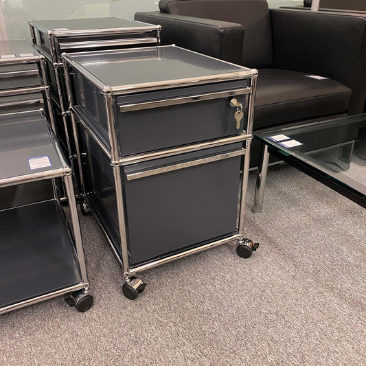USM Haller anthracite roll container with two drawers on casters next to a sofa and glass table