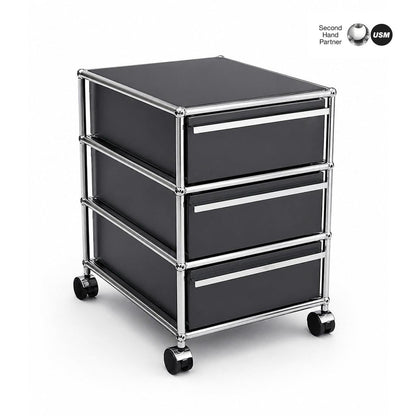 USM Haller Rollcontainer anthrazit mit 3 Schubladen, Chromgestell und Rollen.