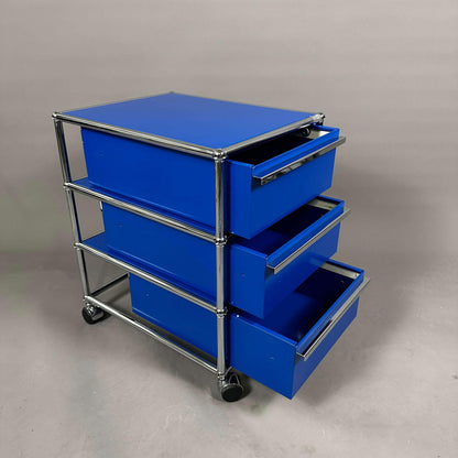 USM Haller Rollcontainer enzianblau mit drei geöffneten Schubladen auf Rollen
