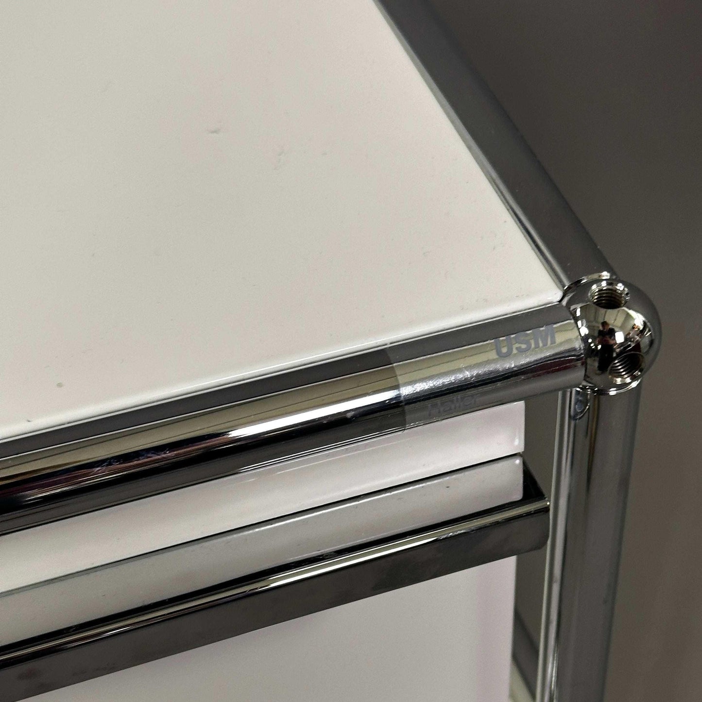 USM Haller Rollcontainer in Reinweiß mit charakteristischem Chrom-Rahmen und markantem Kugelgelenk-Design.