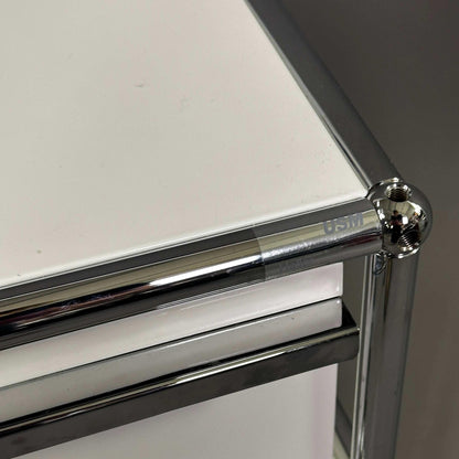 USM Haller Rollcontainer in Reinweiß mit charakteristischem Chrom-Rahmen und markantem Kugelgelenk-Design.