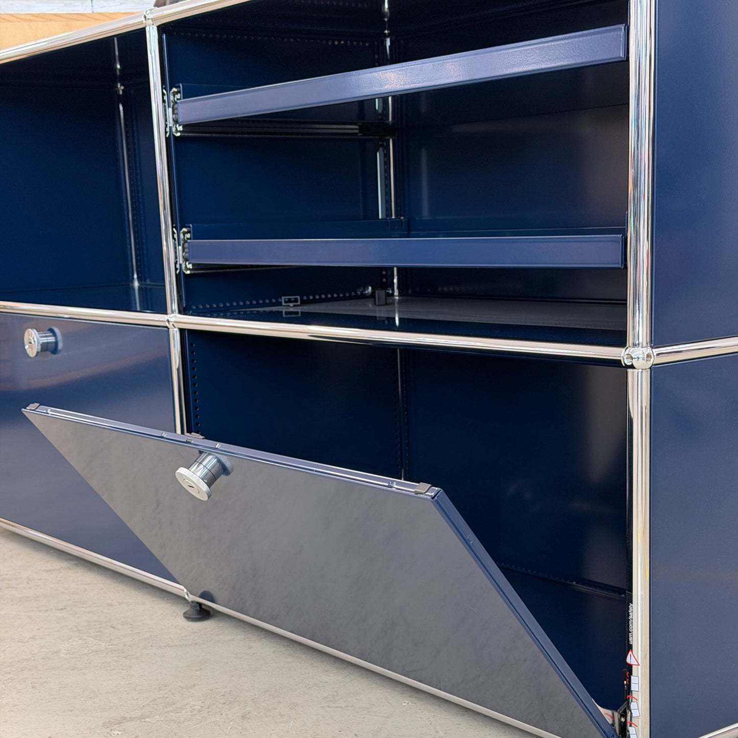 USM Haller Sideboard 2x2 in stahlblau mit offenen Klappen, Ausziehtablaren und Chromrahmen.