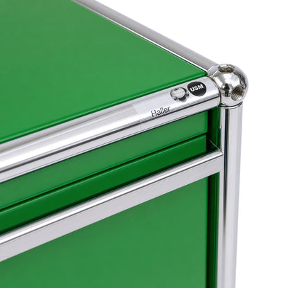 Grünes USM Haller Sideboard mit charakteristischem verchromtem Stahlrohrrahmen und USM-Markenlogo.