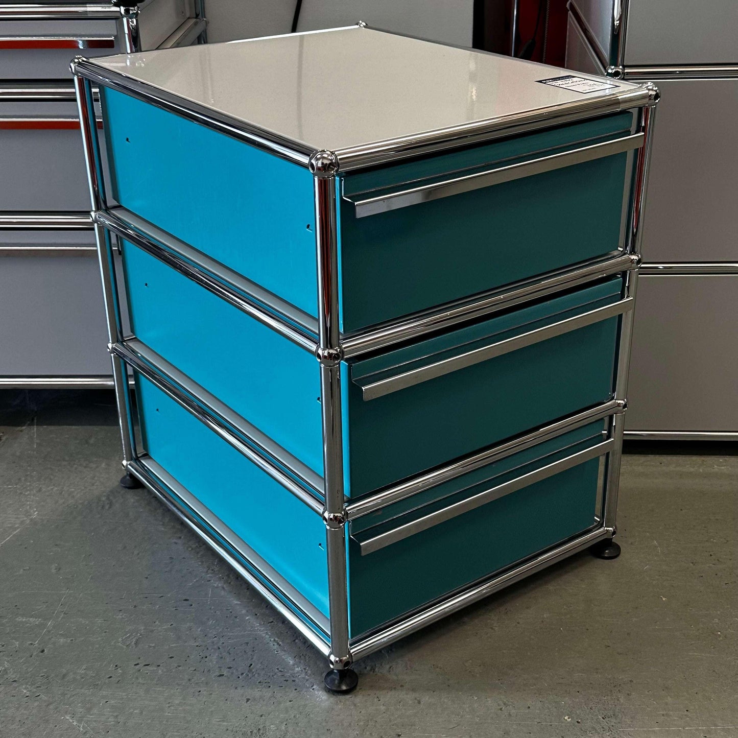 USM Haller Standcontainer with three turquoise drawers and light gray top panel in metal frame
