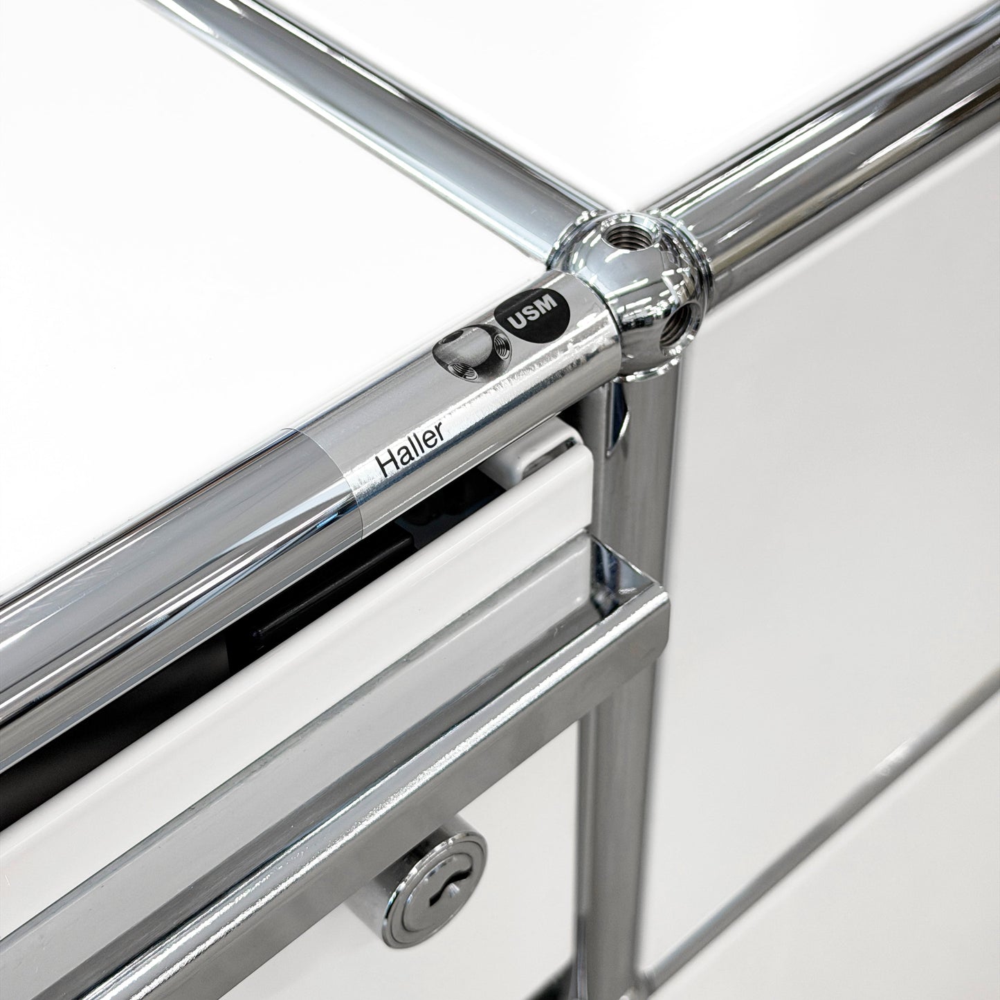 Close-up of USM Haller Technikregal in white, showing chrome frame, "Haller USM" detail, and lock.