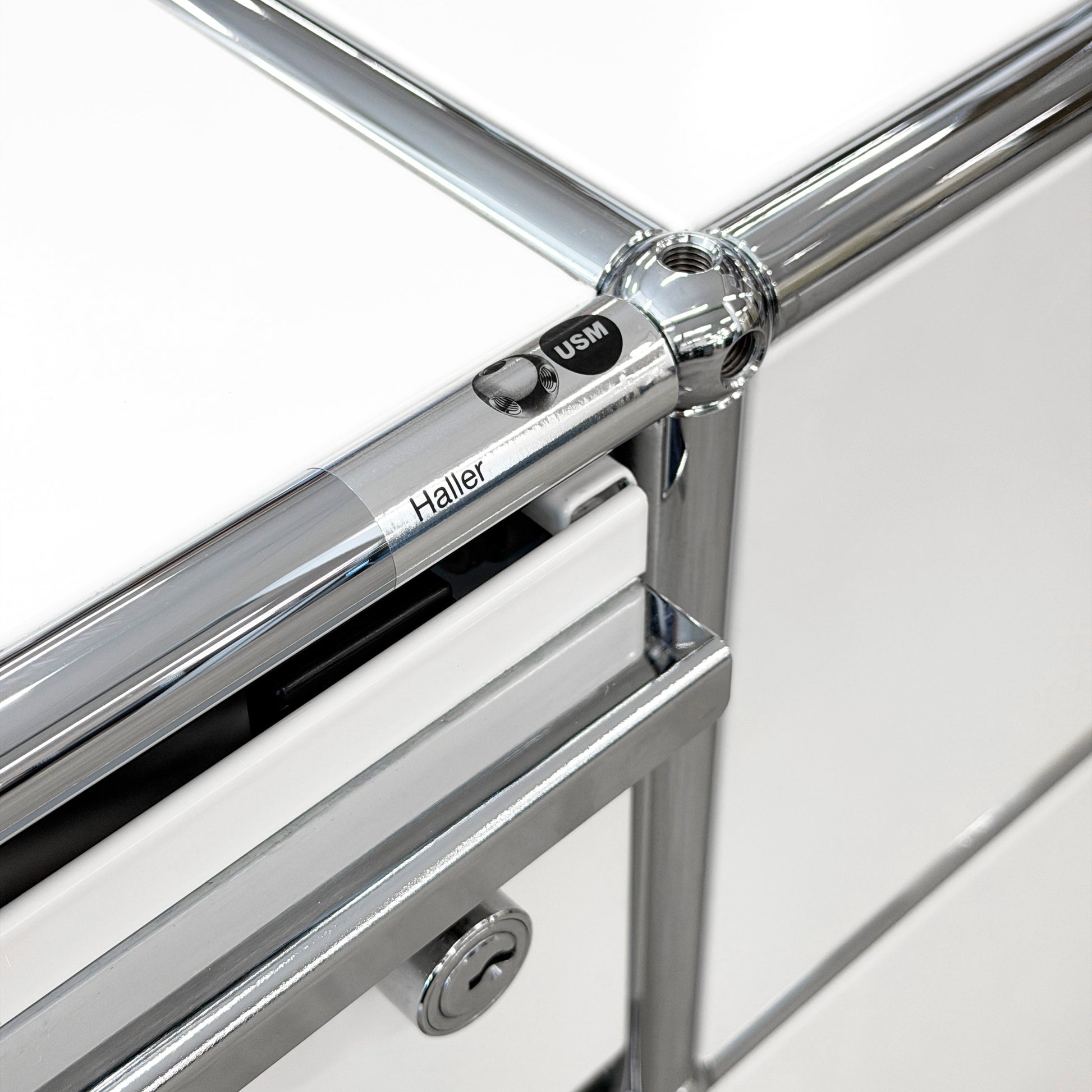 Close-up of USM Haller Technikregal in white, showing chrome frame, "Haller USM" detail, and lock.