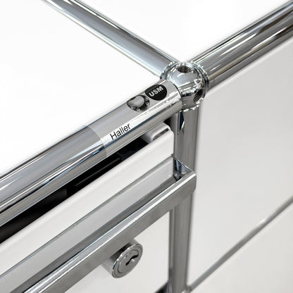 Close-up of USM Haller Technikregal in white, showing chrome frame, "Haller USM" detail, and lock.