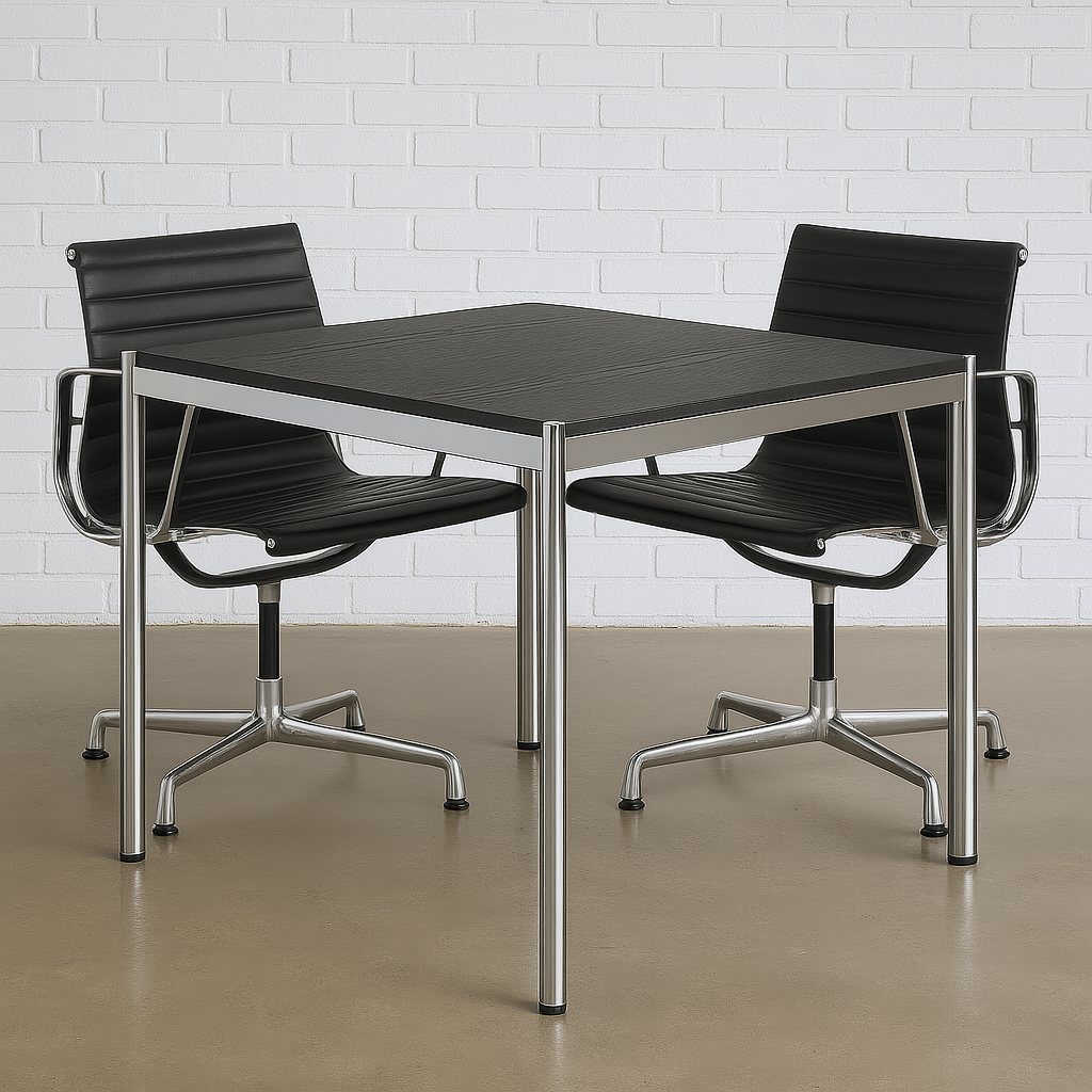 USM Haller Tisch 100x100cm schwarzes Eichenfurnier mit Chromgestell, moderner Arbeitstisch mit zwei schwarzen Bürostühlen vor weißer Ziegelwand