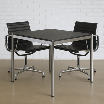 USM Haller Tisch 100x100cm schwarzes Eichenfurnier mit Chromgestell, moderner Arbeitstisch mit zwei schwarzen Bürostühlen vor weißer Ziegelwand