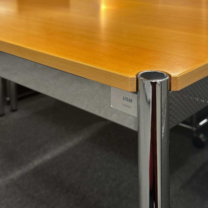 USM Haller Tisch 125x75 aus Buche natur mit glänzenden Chrombeinen und USM Haller Logo.