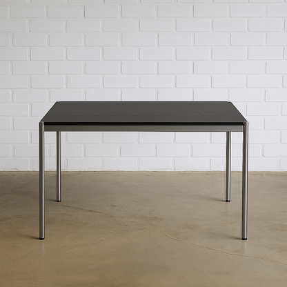 USM Haller Tisch 125x75cm mit schwarzer Eichenplatte und Chromgestell vor weißer Ziegelwand