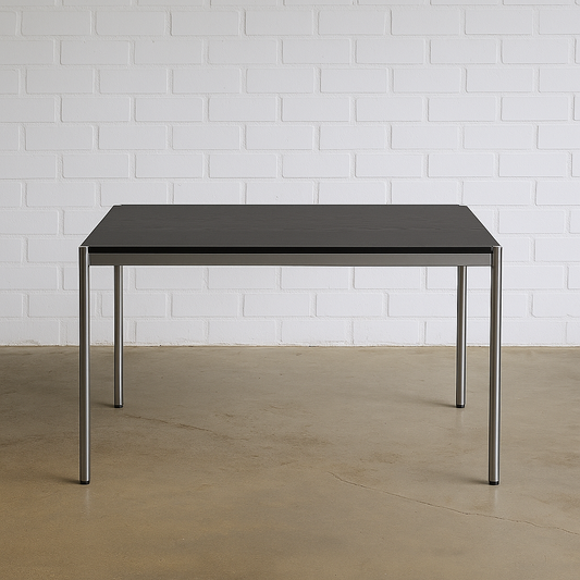 USM Haller Tisch 125x75cm mit schwarzer Eichenplatte und Chromgestell vor weißer Ziegelwand