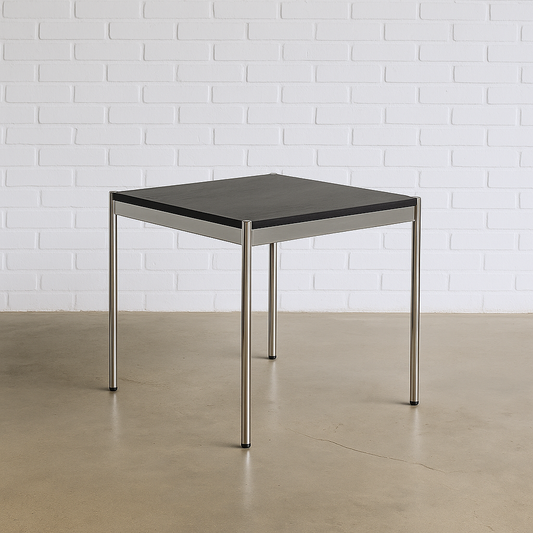 USM Haller Tisch 75x75 cm mit schwarz lackierter Eichenplatte und chromfarbenem Gestell vor weißer Backsteinwand