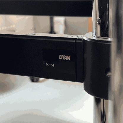 Close-up of USM Kitos E2 electric height-adjustable desk frame in black with logo and metal support details.