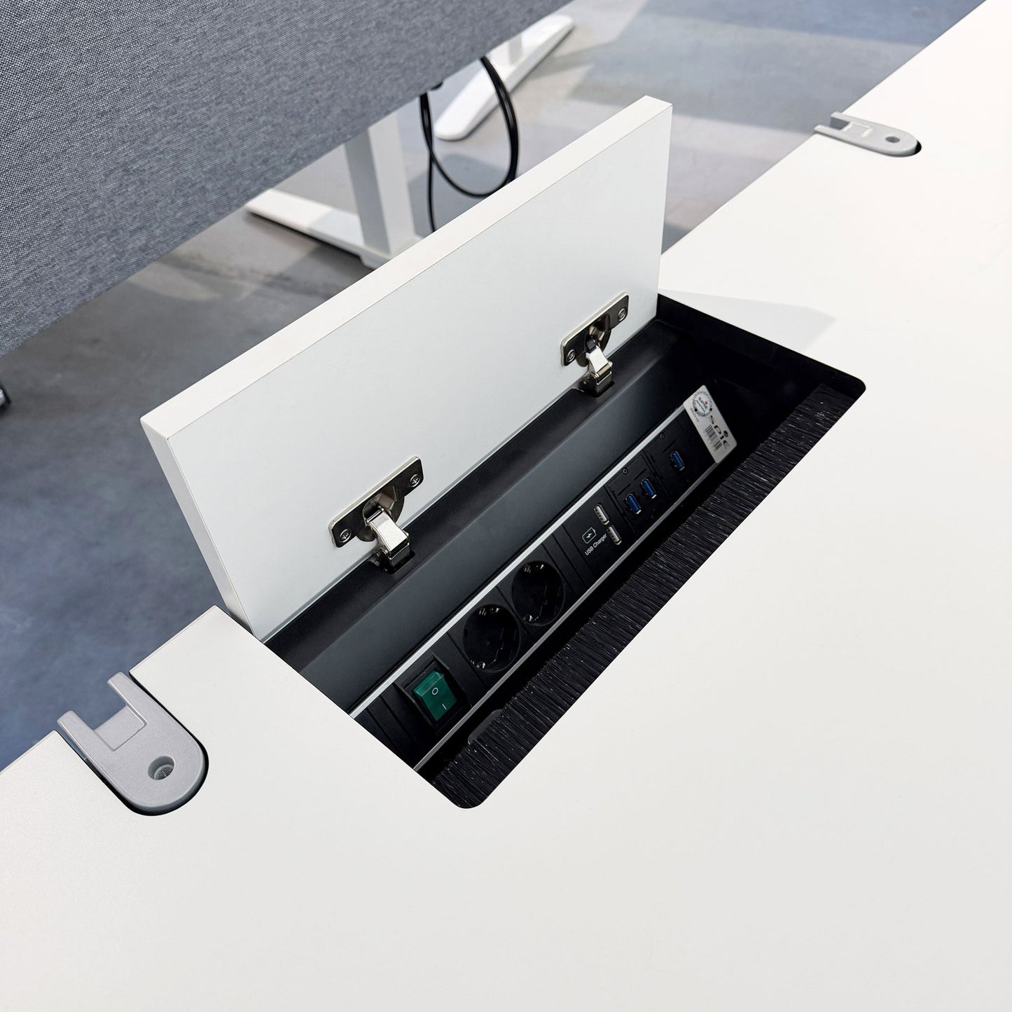 Geöffnete Kabelklappe mit Steckdosen und USB-Ports im VS Serie 901 Schreibtisch in Weiß.