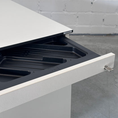 Weißer Vario Rollcontainer mit schwarzer Kante und ausgezogener Stiftschublade inklusive Schloss.