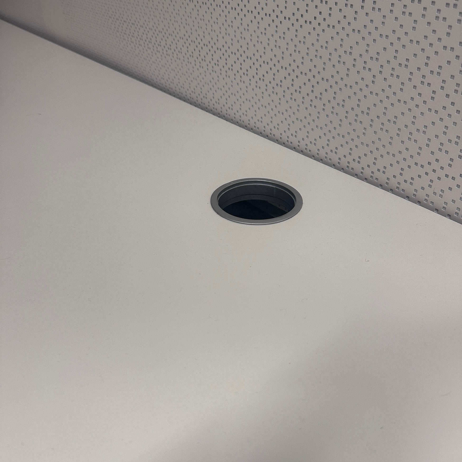 Close-up of Vario Stage Schreibtisch white tabletop with black-edged cable grommet and gray patterned background
