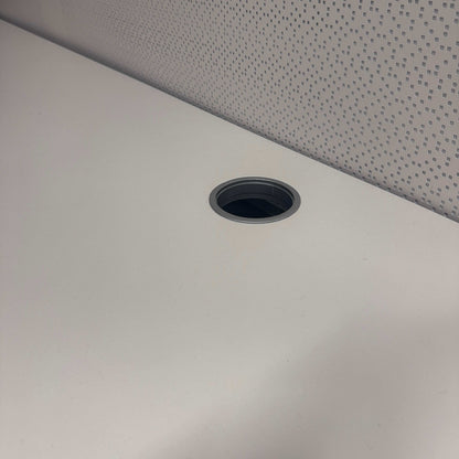Close-up of Vario Stage Schreibtisch white tabletop with black-edged cable grommet and gray patterned background